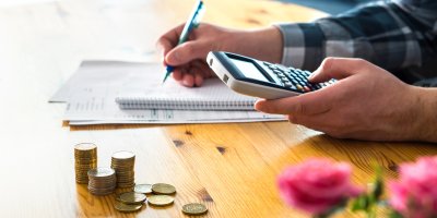 Muž si počítá finance na papíru a kalkulačce, vedle něj leží hromádka peněz