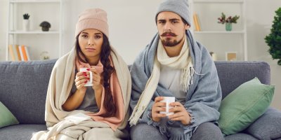 Muž a žena zabalení v dece a šále, na hlavě mají čepice a drží hrnky