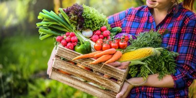 Žena nese bedýnku s čerstvou zeleninou