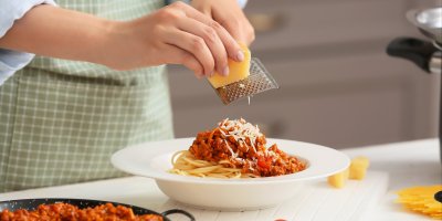 Žena strouhá sýr na talíř špaget s masovou směsí