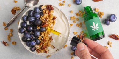Ruka kapající CBD kapky do talíře s jogurtem, ovocem a müsli