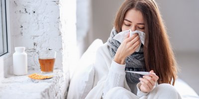 Nemocná smrkající žena s čajem a teploměrem