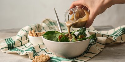 Člověk lije tahini do misky se salátem