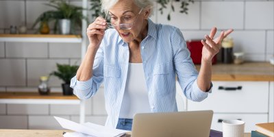 Starší žena se překvapeně dívá na list papíru u notebooku