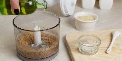 V mixéru jsou sezamová semínka, člověk k nim přilévá olej, vedle je v jedné mističce sůl a v druhé semínka