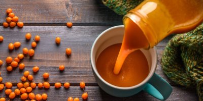 Sirup je naléván do hrnečku a vedle jsou kuličky rakytníku