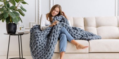 Žena sedící na gauči, přikrytá robustní pletenou dekou
