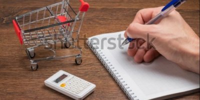 Ruka s propiskou nad sešitem; vedle ní malá kalkulačka a nákupní vozík