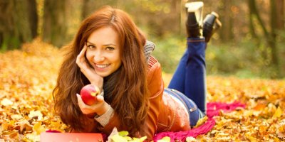 žena leží v podzimním listí a drží jablko
