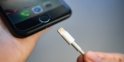 Člověk strká nabíječku s konektorem Lightning do mobilního telefonu od Applu