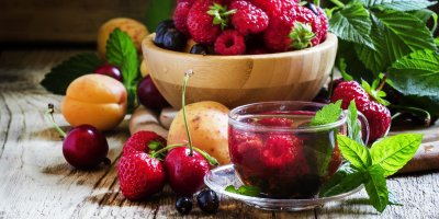 Pečený čaj z malin a jahod v hrnku, v pozadí mísa plná lesního ovoce