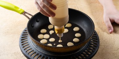 Žena připravuje mini palačinky dávkovačem s těstem na pánev