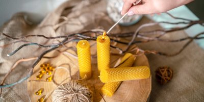 Člověk zapaluje svíčku z včelího vosku, další tři jsou nezapálené