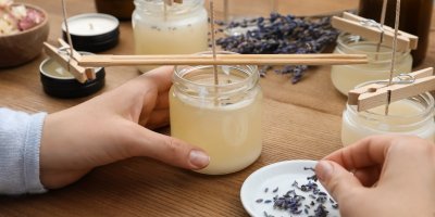 Člověk vyrábí svíčky, jednu drží v ruce a druhou rukou nabírá sušené květy