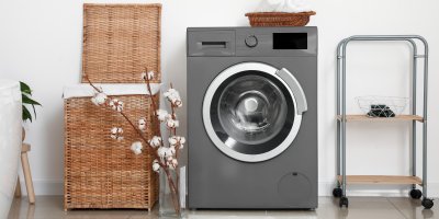 Šedá pračka, proutěný koš na prádlo, váza s bavlníkem