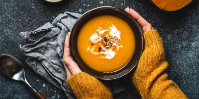 Žena ve svetru drží misku s dýňovým krémem