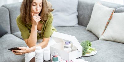 Žena zklamaně kouká na potraviny a doplňky stravy s telefonem v ruce