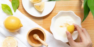 Miska se syrovým mlékem, do kterého žena vymačkává šťávu z citronu, vedle jsou citrony a mistička s medem