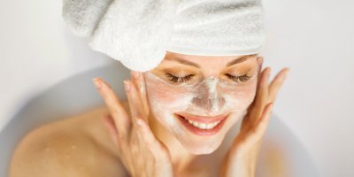 Žena leží ve vaně a na obličeji si rozmazává pleťovou masku z mléka