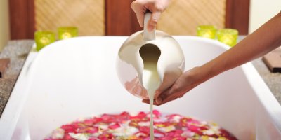 Vana plná okvětních plátků růží, do níž člověk přilévá mléko ze džbánu