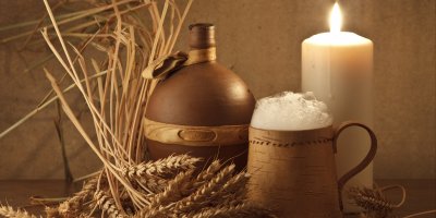 Dřevěný korbel s pivem, kožená čutora a hořící svíce