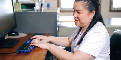 Slepá žena pracuje s počítačem pomocí speciální klávesnice