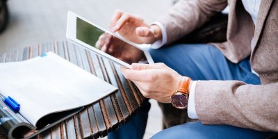 Muž pracuje na tabletu, na stolku má otevřený časopis