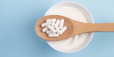 Miska s bílým jogurtem, na které je položená lžíce s probiotiky v kapslích