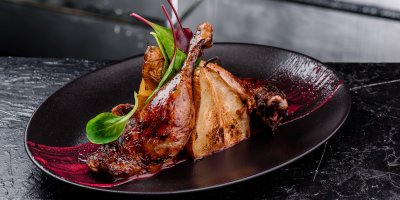 Husí stehna s červenou omáčkou a pečenou hruškou, servírovaná na černém talíři