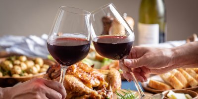 Dva lidé si připíjejí vínem nad talíři s pečenou husou, brambory a dalšími pokrmy