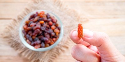 Ruka drží jednu světlou rozinku, v misce pod ní je směs zlatých a hnědých rozinek