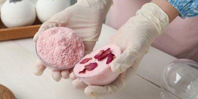 Člověk vyrábí koupelovou bombu, drží dvě formičky, ve kterých je růžová hmota a okvětní lístky 