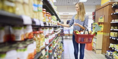 Žena s košíkem nakupuje v supermarketu mezi regály