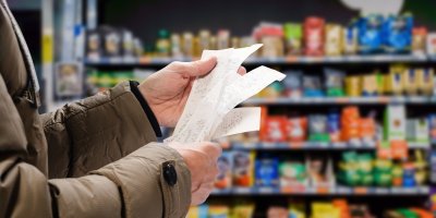Člověk v zimě bundě si v supermarketu prohlíží účtenky