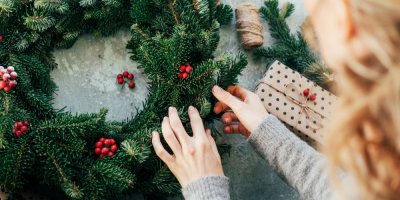 Žena vyrábí vánoční věnec, připevňuje na něj plody cesmíny