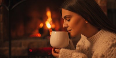Žena ve svetru drží v rukou hrnek s horkým nápojem