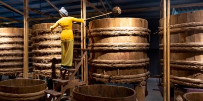 Žena v muzeu ukazuje, jak se lila omáčka do dřevěných kádí