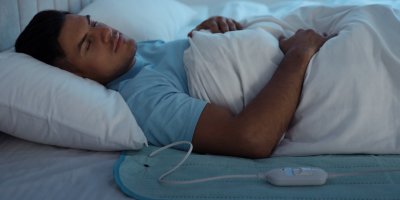 Spící muž leží v posteli na vyhřívací podložce