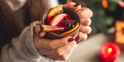 Žena ve svetru držící hrnek punče s ovocem a kořením