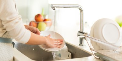 Žena myje nádobí pod tekoucí vodou