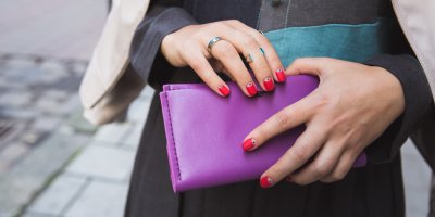 Žena s růžovými nehty drží výraznou fialovou peněženku