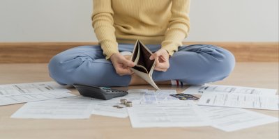 Žena s prázdnou peněženkou a kalkulačkou sedí na zemi obklopená listy papíru