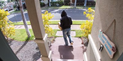 Zloděj odnášející balíček od vchodových dveří