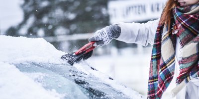 Žena čistí čelní sklo auta smetáčkem na sníh