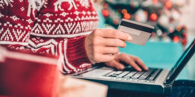 Žena ve vánočním svetru s kreditní kartou u notebooku
