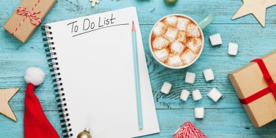 Otevřený kroužkový sešit s nápisem To Do List, kolem jsou vánoční ozdoby, dárky a horká čokoláda s marshmallow