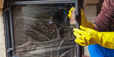 Muž v gumových rukavicích čistí krbové sklo