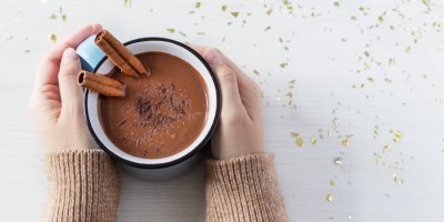 Ruce svírají hrnek s horkou čokoládou se skořicí