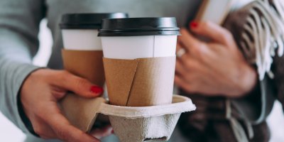 Žena držící dva kelímky s kávou v papírovém podnosu