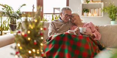 Starší muž a žena přikrytí dekou sedí na sedačce před vánočním stromkem